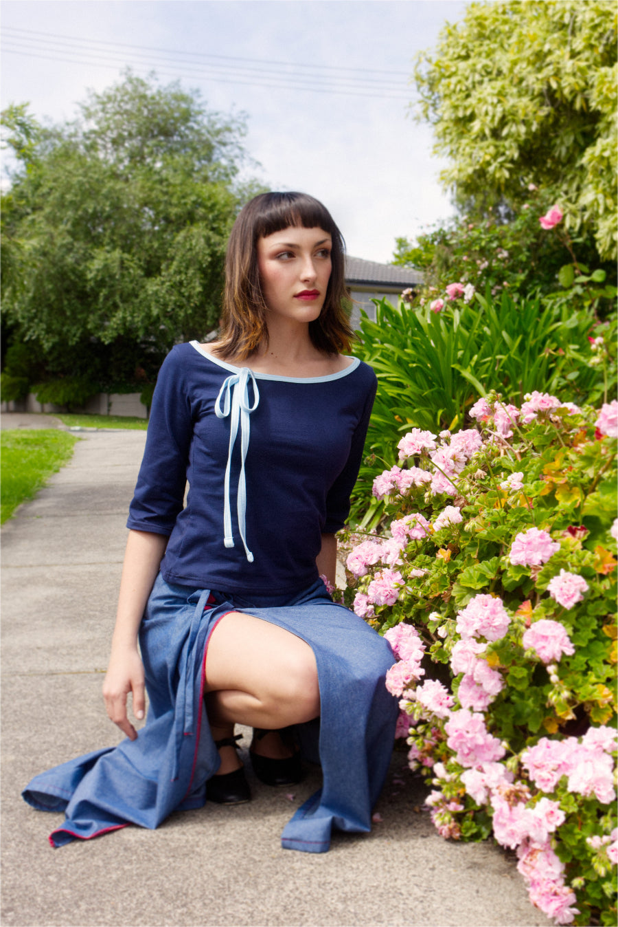 Woman in a blue dress sitting on a path with flowers and trees in the background