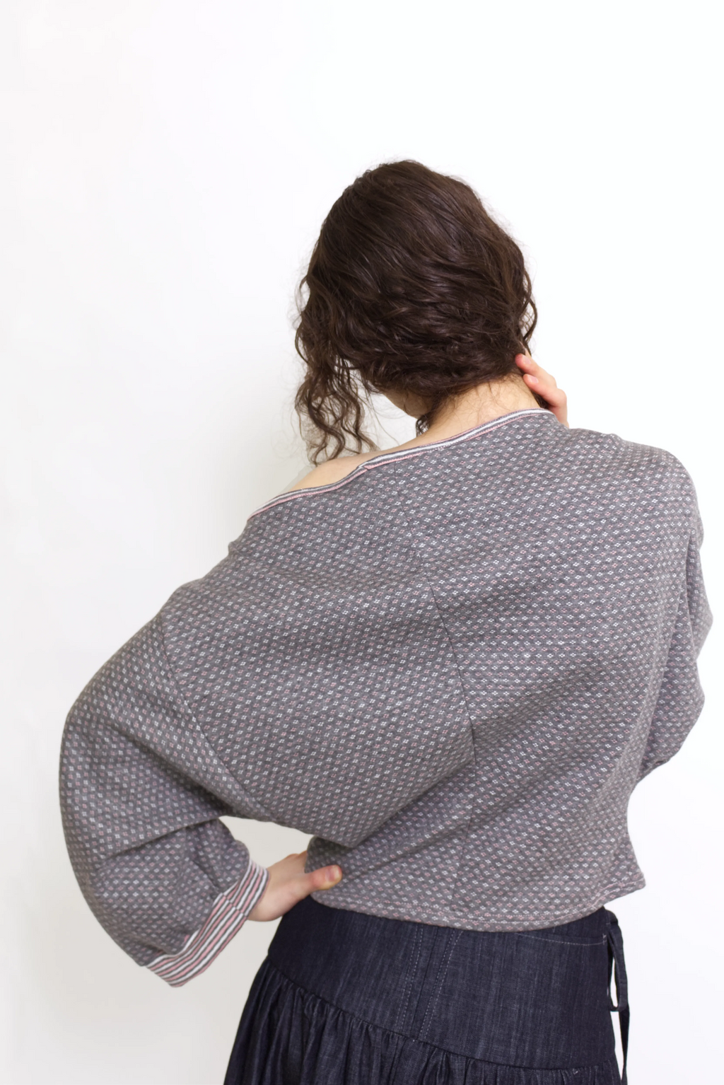 young woman wearing a gray, pink and white patterned oversized cotton boat neck pullover top, with long sleeves on a white background