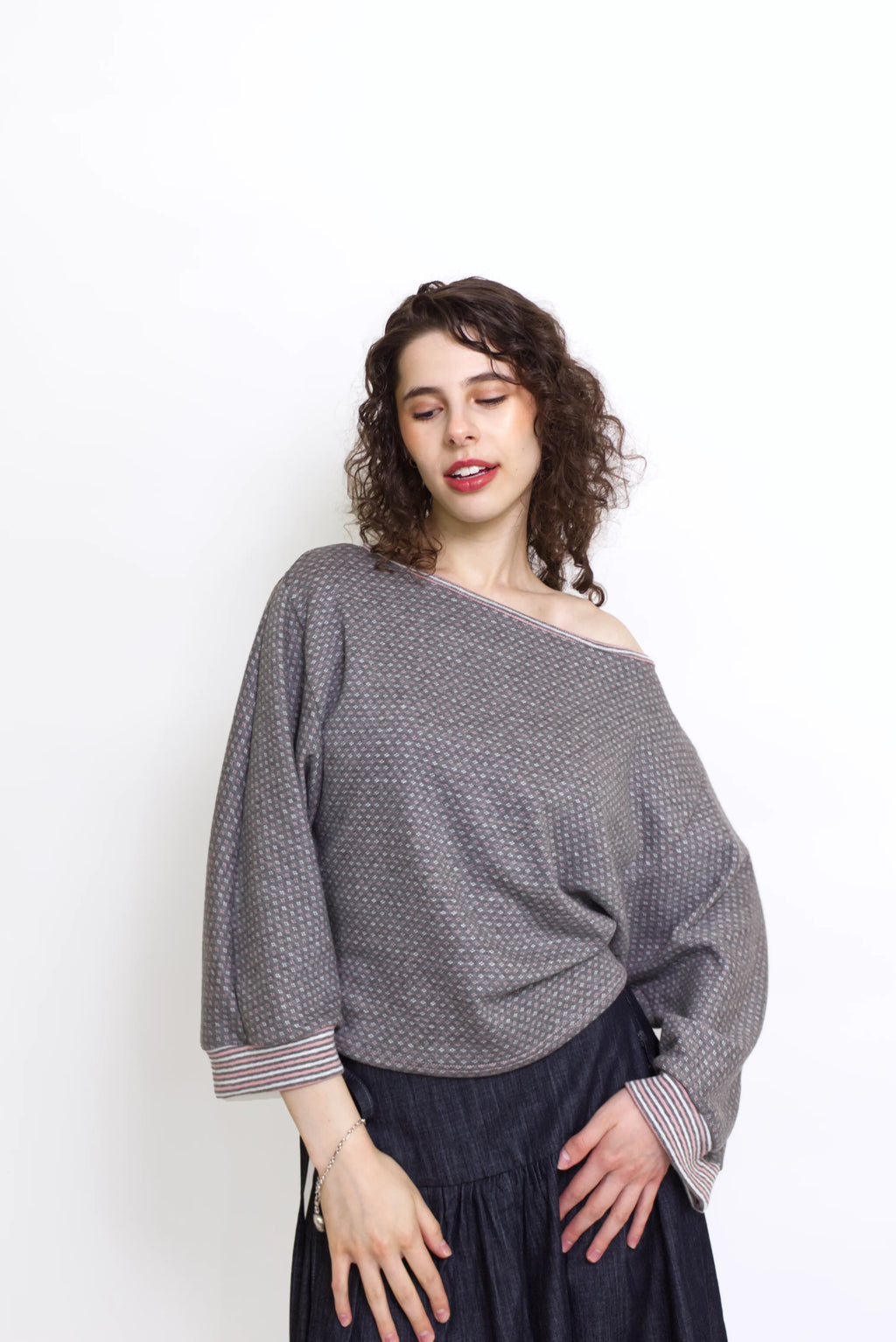 young woman wearing a gray, pink and white patterned oversized cotton boat neck pullover top, with long sleeves on a white background