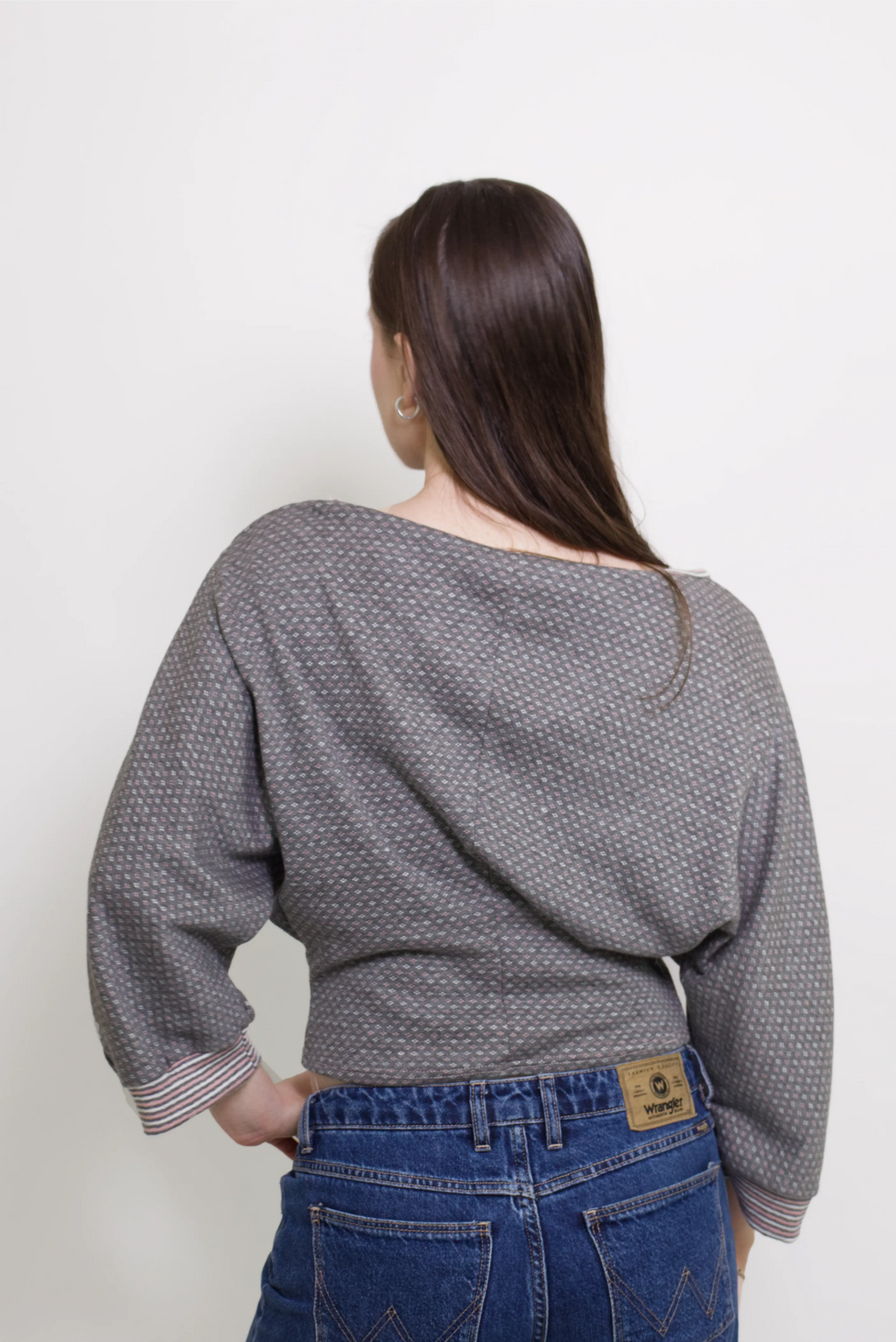 young woman wearing a gray, pink and white patterned oversized cotton boat neck pullover top, with long sleeves on a white background
