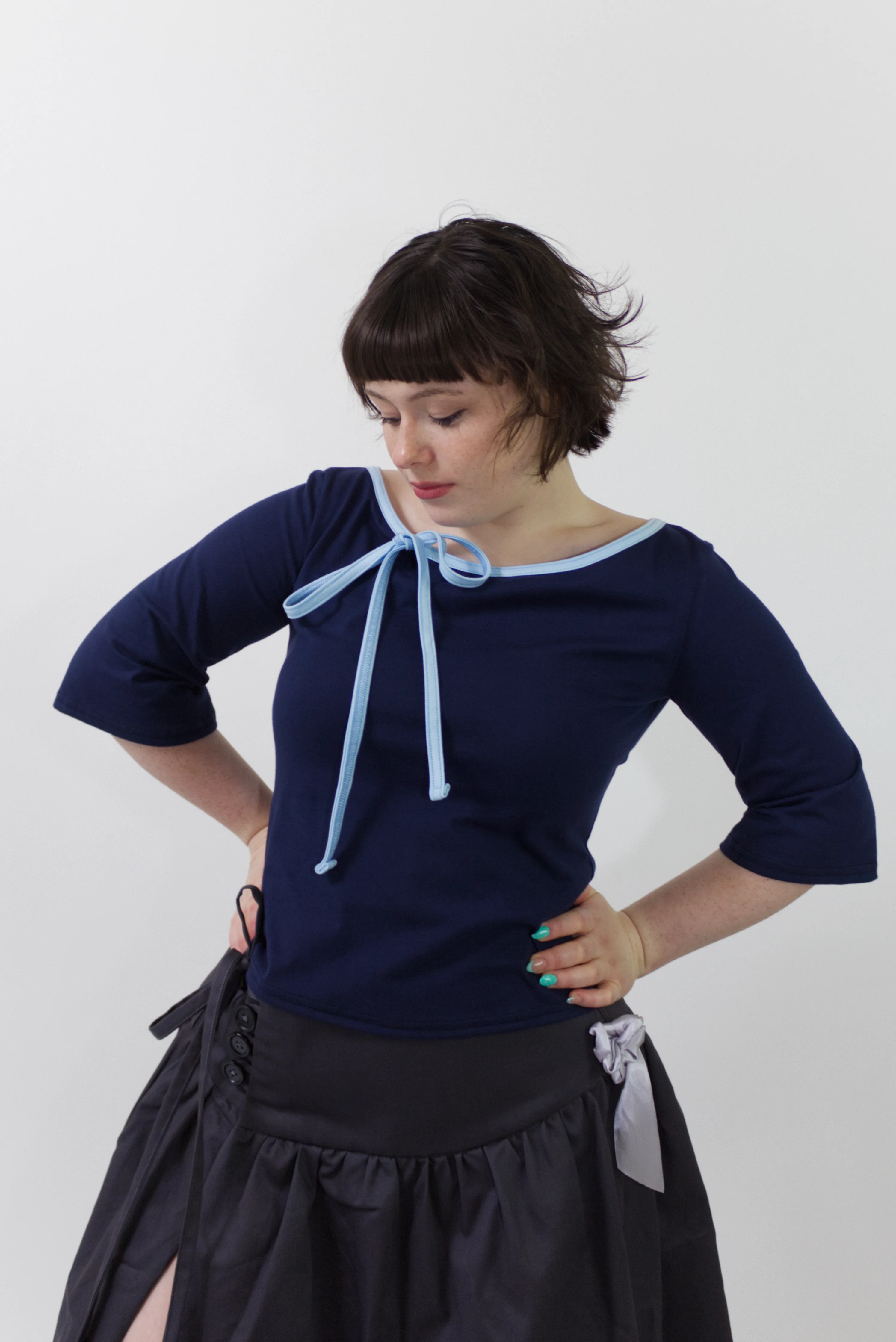 Woman wearing a navy blue top with a light blue ribbon and a black skirt against a white background