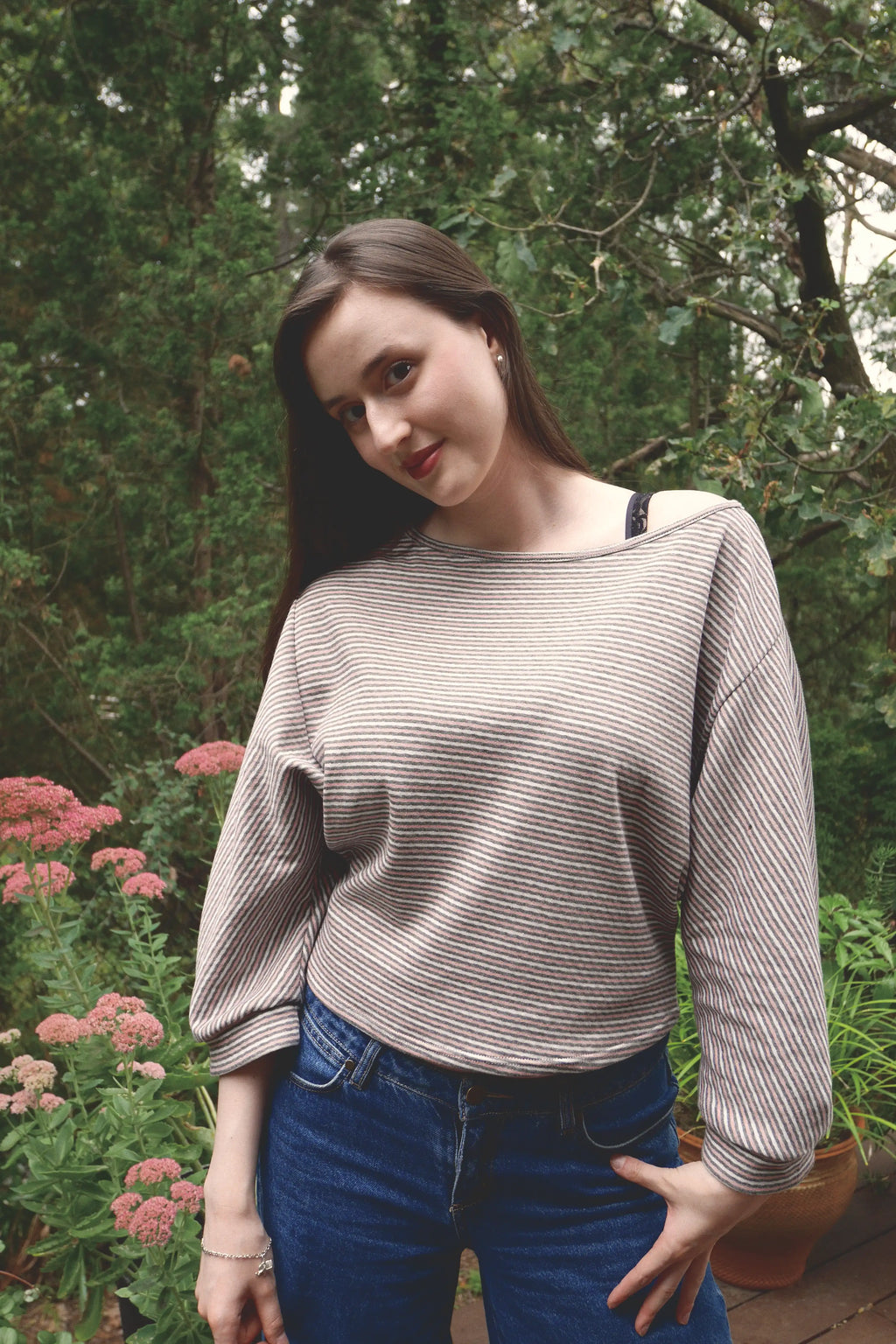 young woman wearing a pink striped oversized cotton boat neck pullover top, with long sleeves outside