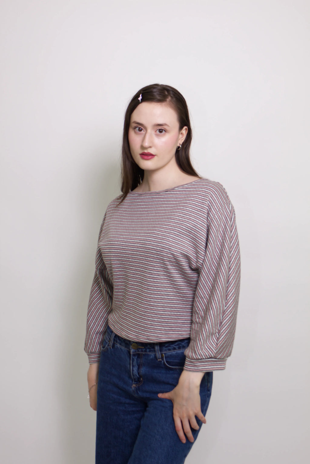 young woman wearing a pink striped oversized cotton boat neck pullover top, with long sleeves on a white background
