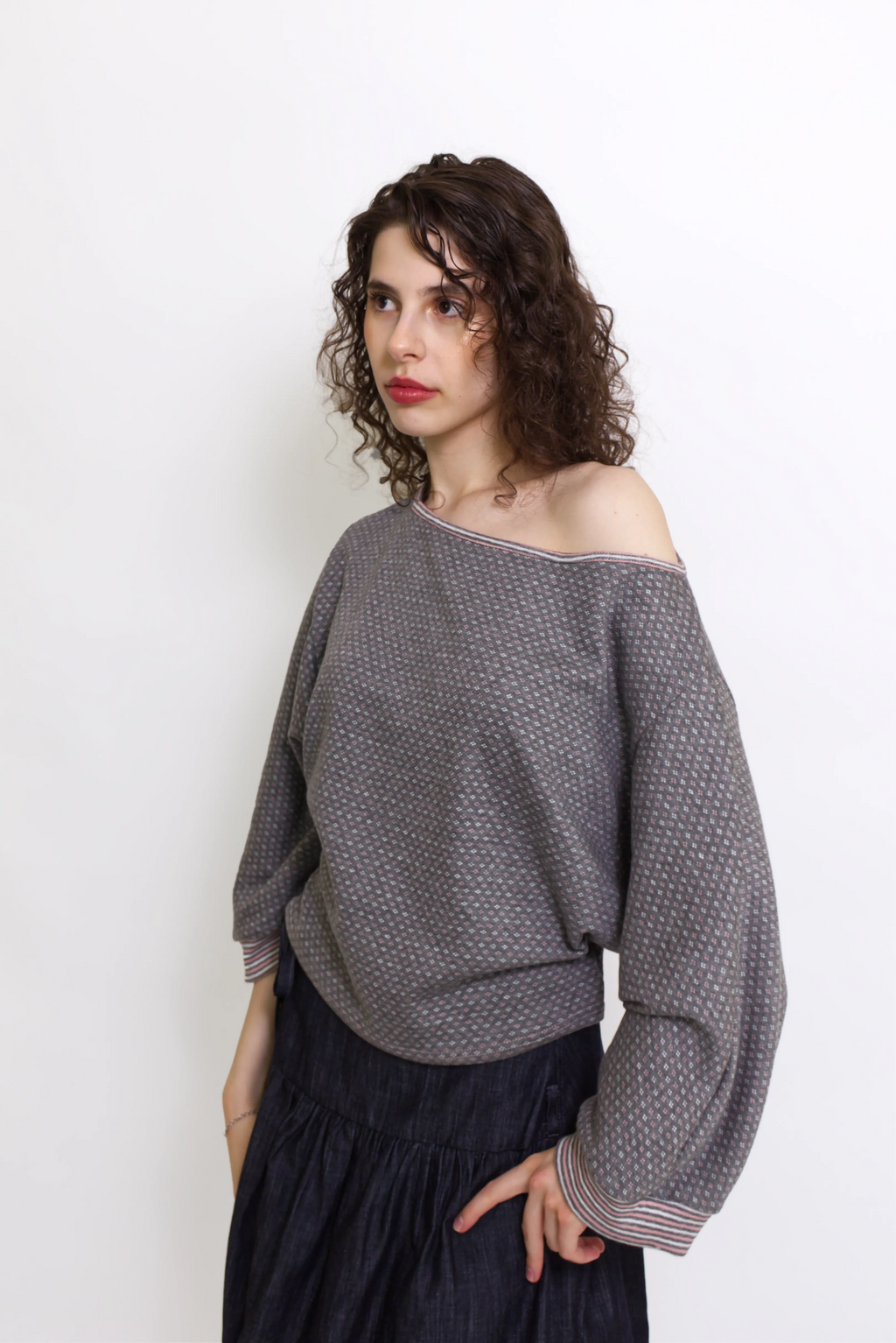 young woman wearing a grey, pink and white patterned oversized cotton boat neck pullover top, with long sleeves on a white background