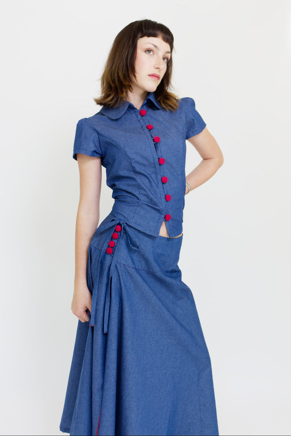 Woman wearing a matching blue blouse and skirt set with red buttons on a white background