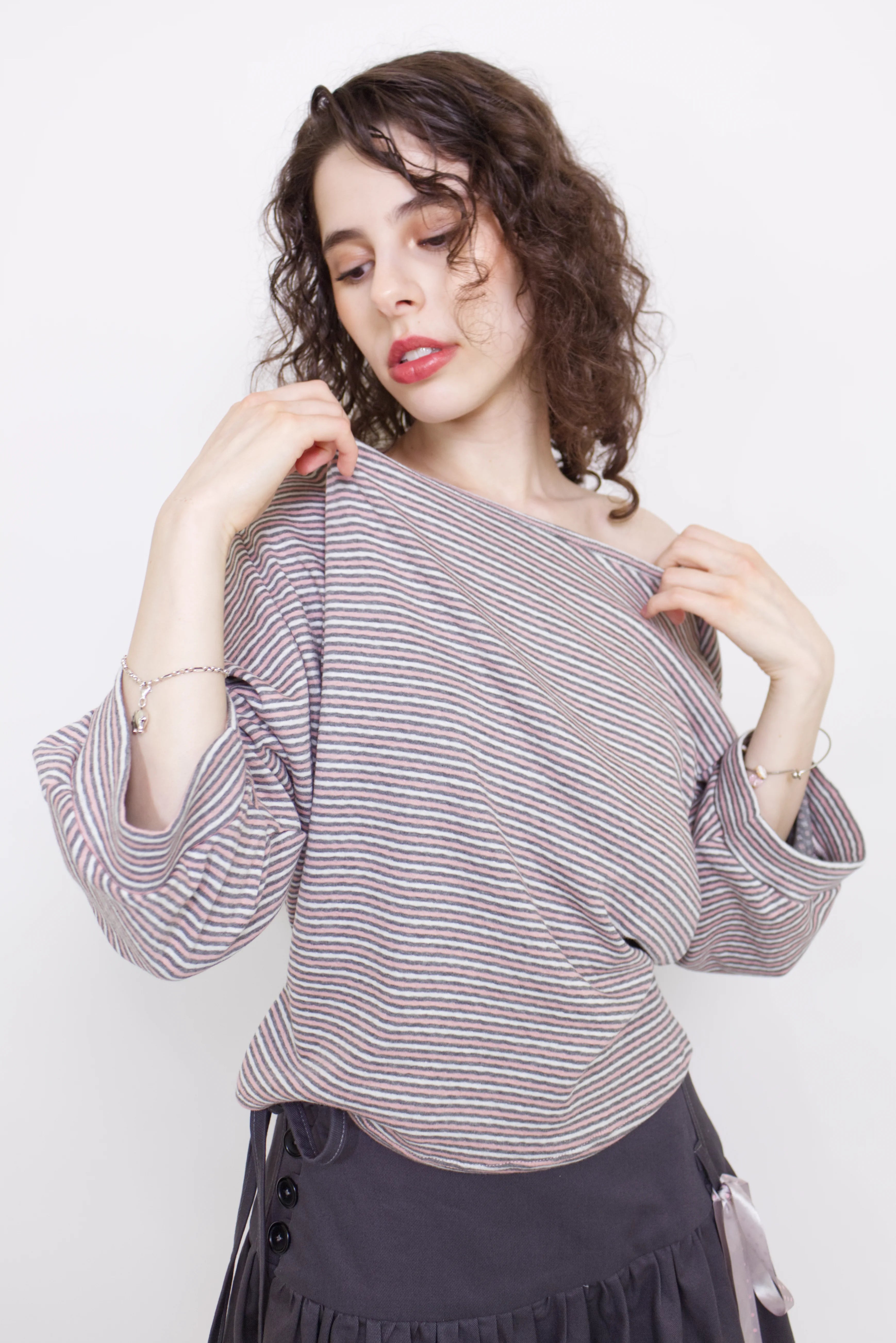 young woman wearing a pink striped oversized cotton boat neck pullover top, with long sleeves on a white background