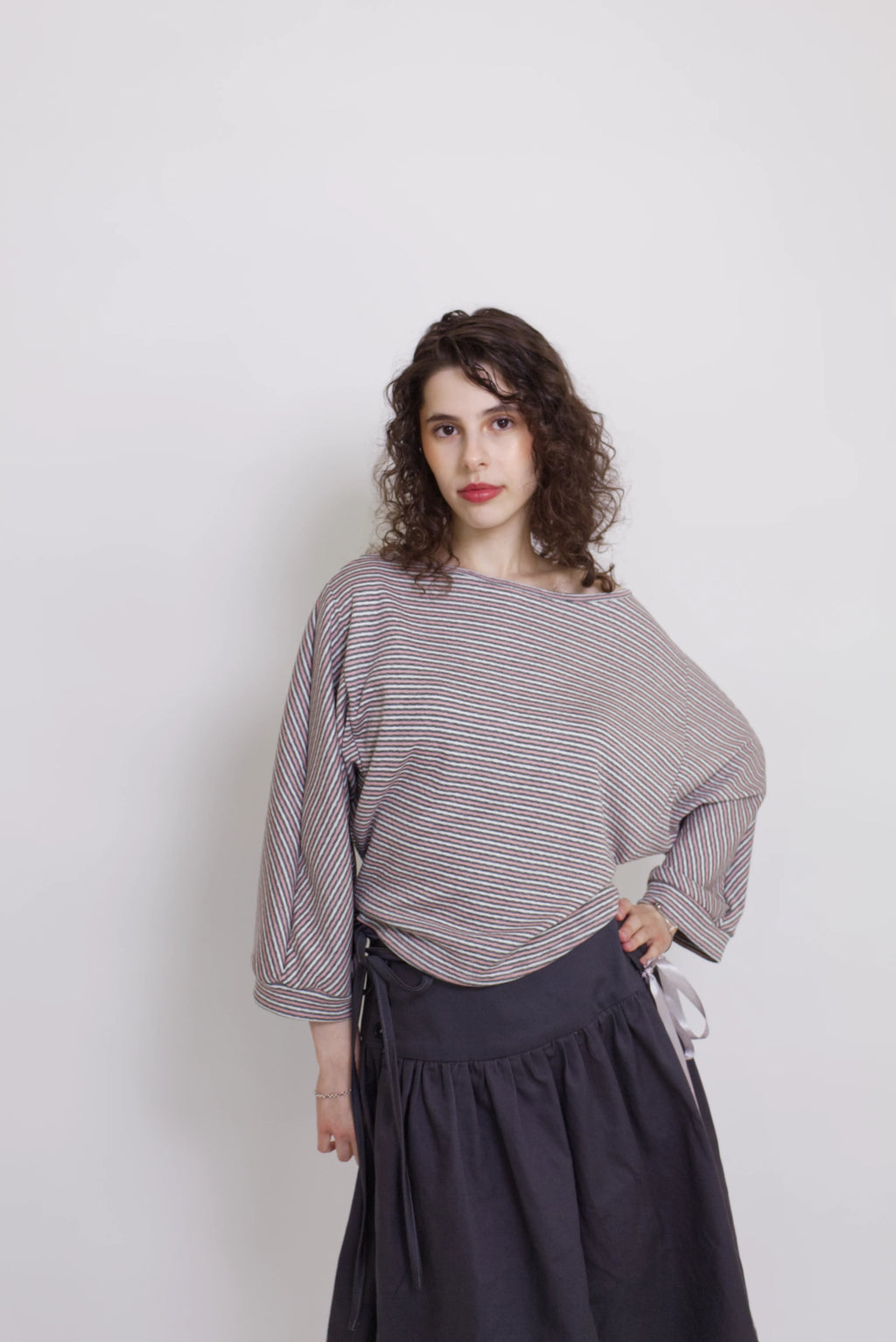 young woman wearing a pink striped oversized cotton boat neck pullover top, with long sleeves on a white background