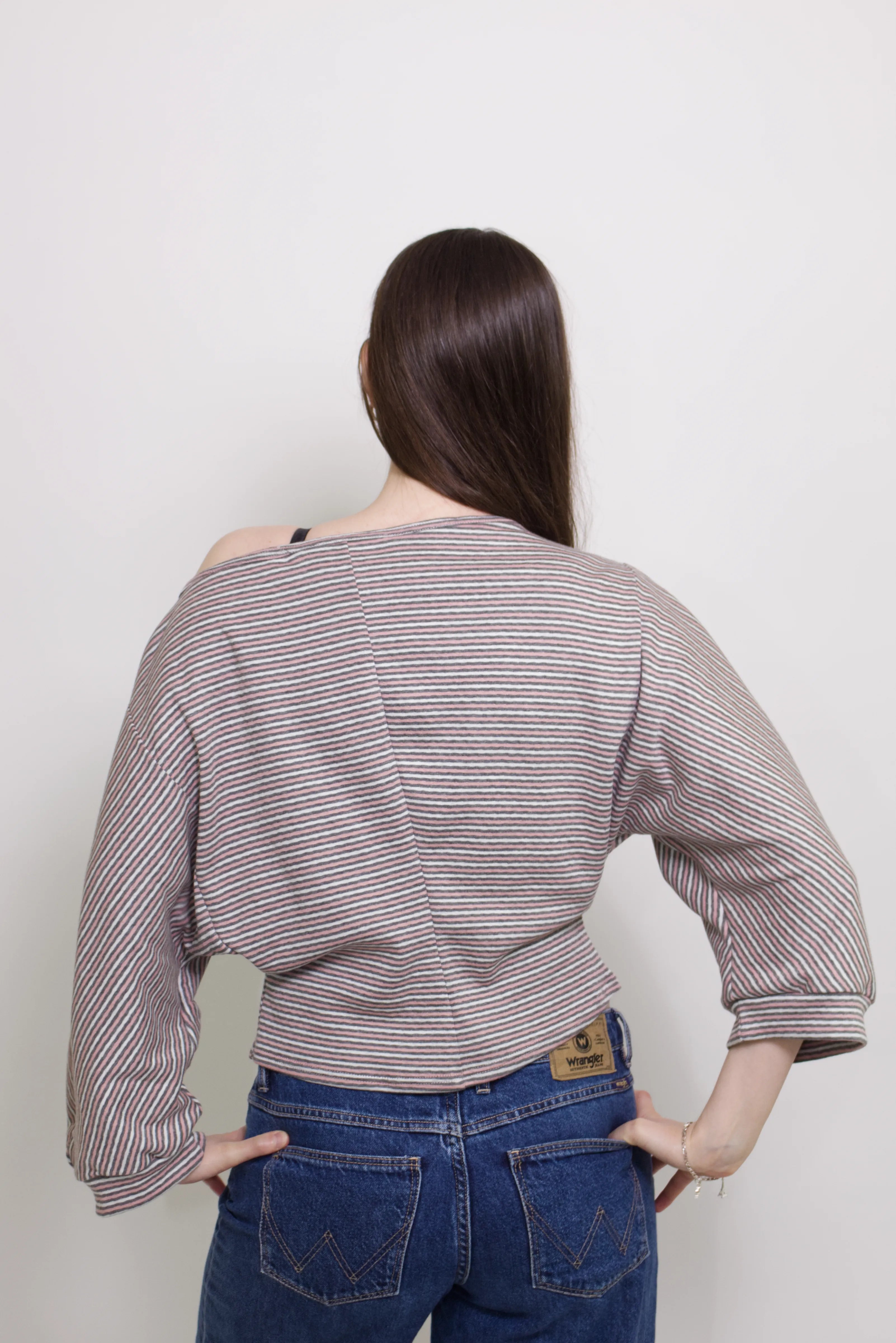 young woman wearing a pink striped oversized cotton boat neck pullover top, with long sleeves on a white background