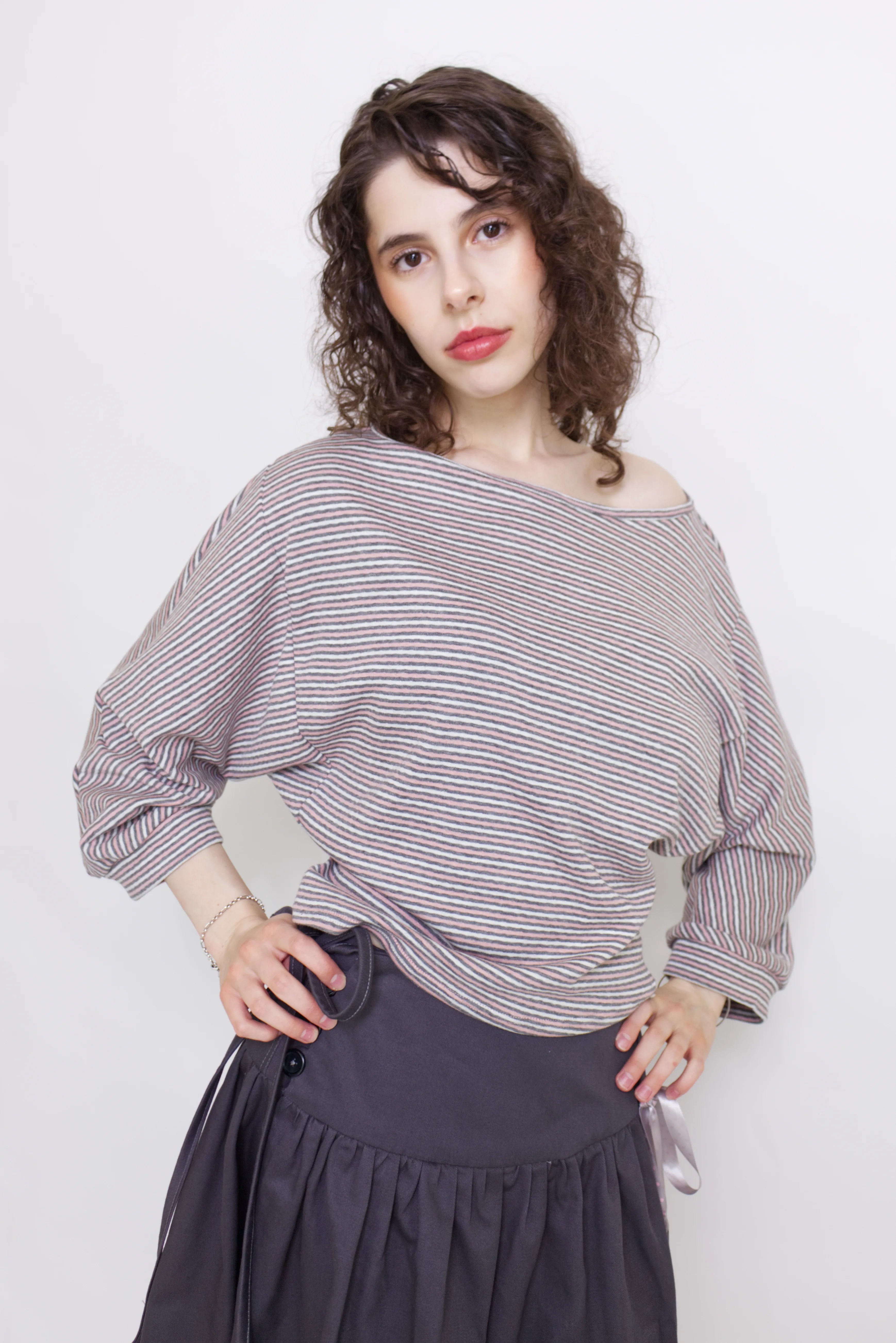 young woman wearing a pink striped oversized cotton boat neck pullover top, with long sleeves on a white background