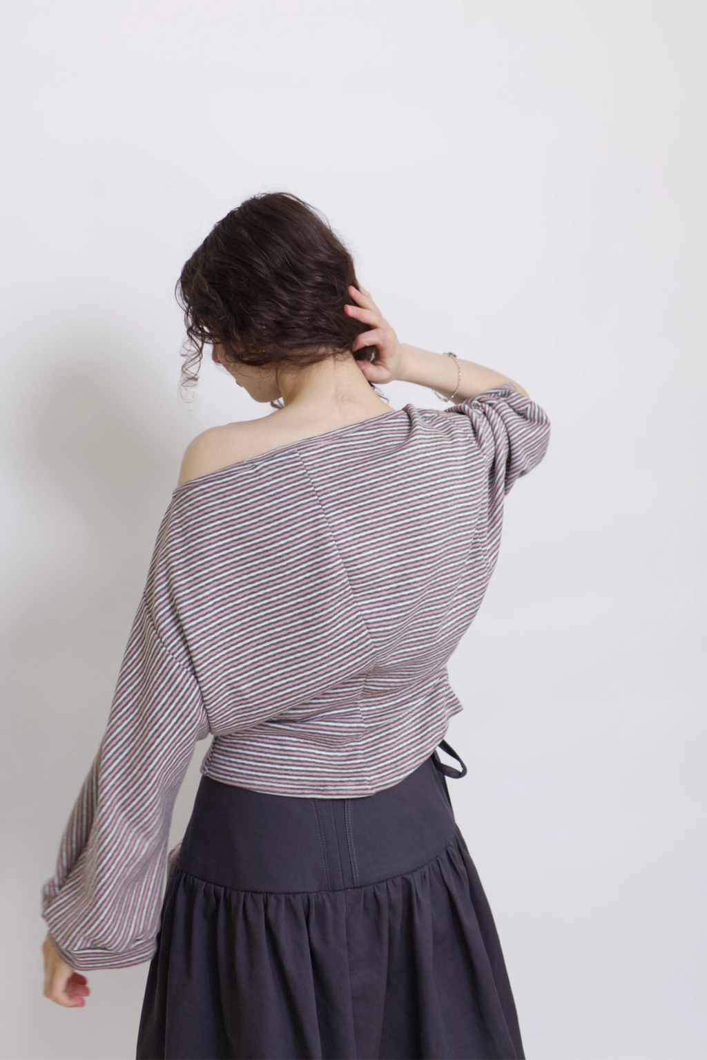young woman wearing a pink striped oversized cotton boat neck pullover top, with long sleeves on a white background