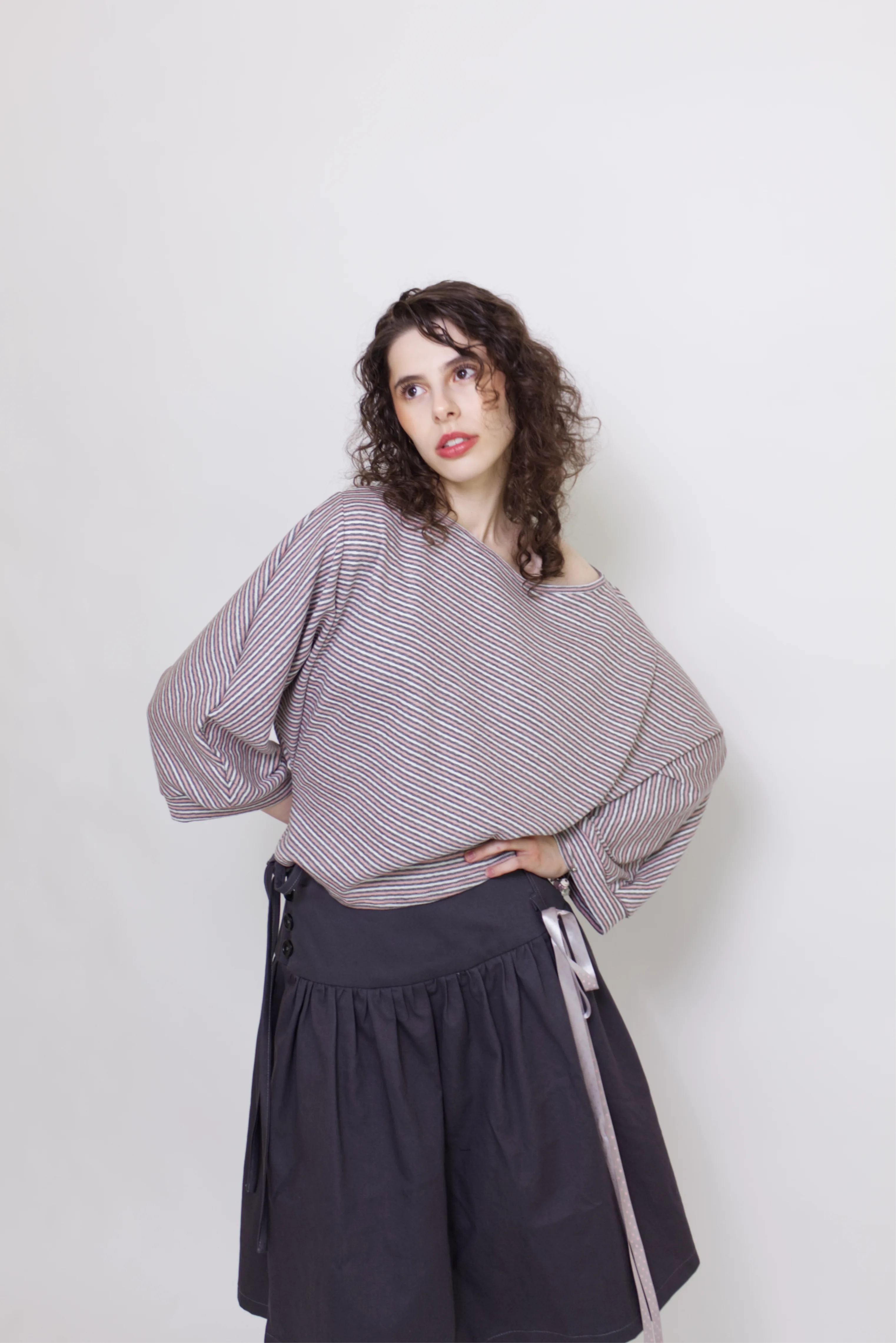 young woman wearing a pink striped oversized cotton boat neck pullover top, with long sleeves on a white background
