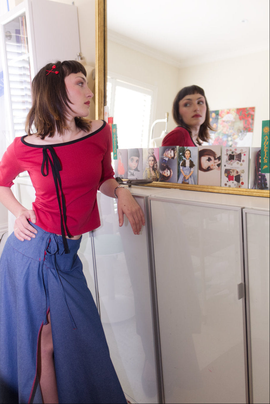 Woman in a red boat neck top and blue denim maxi skirt standing in front of a mirror.